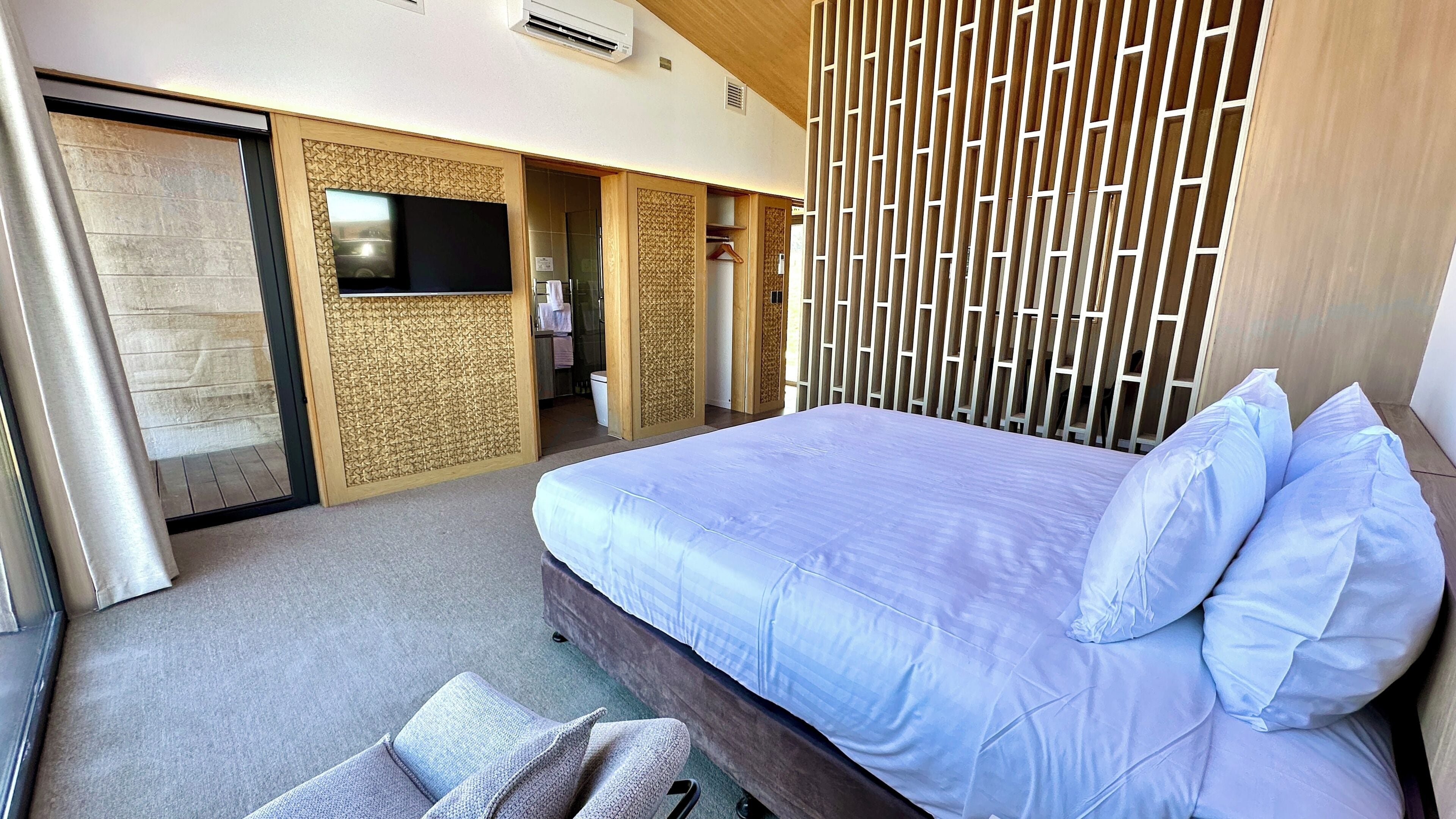 Een moderne hotelkamer met een groot bed, een flatscreen televisie, een kledingkast en een schuifdeur.