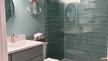 Une salle de bain avec une douche à parois de verre, un lavabo avec un miroir et des toilettes.