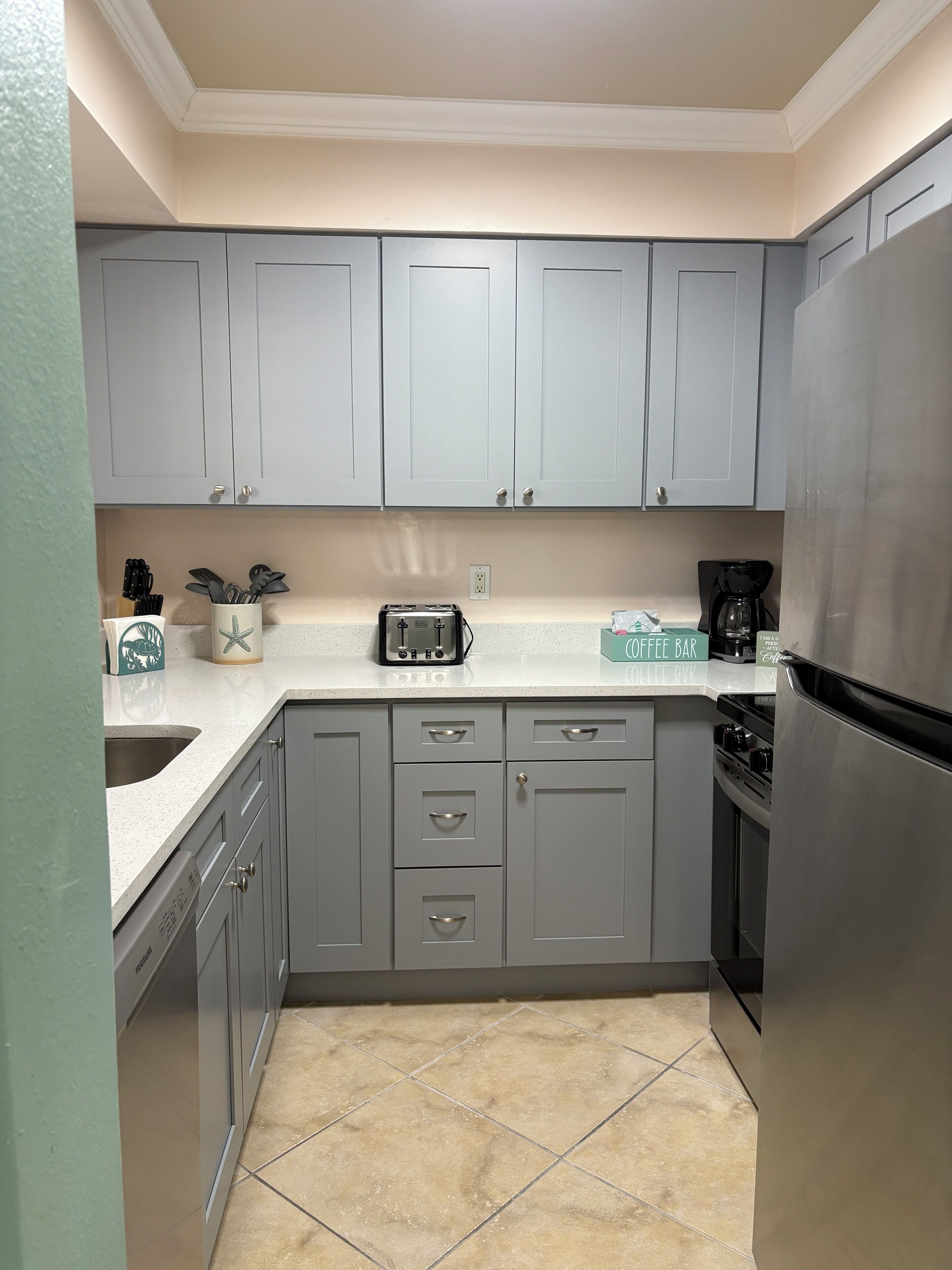 A kitchen with grey cabinets, a stainless steel refrigerator, a coffee maker, and a toaster.