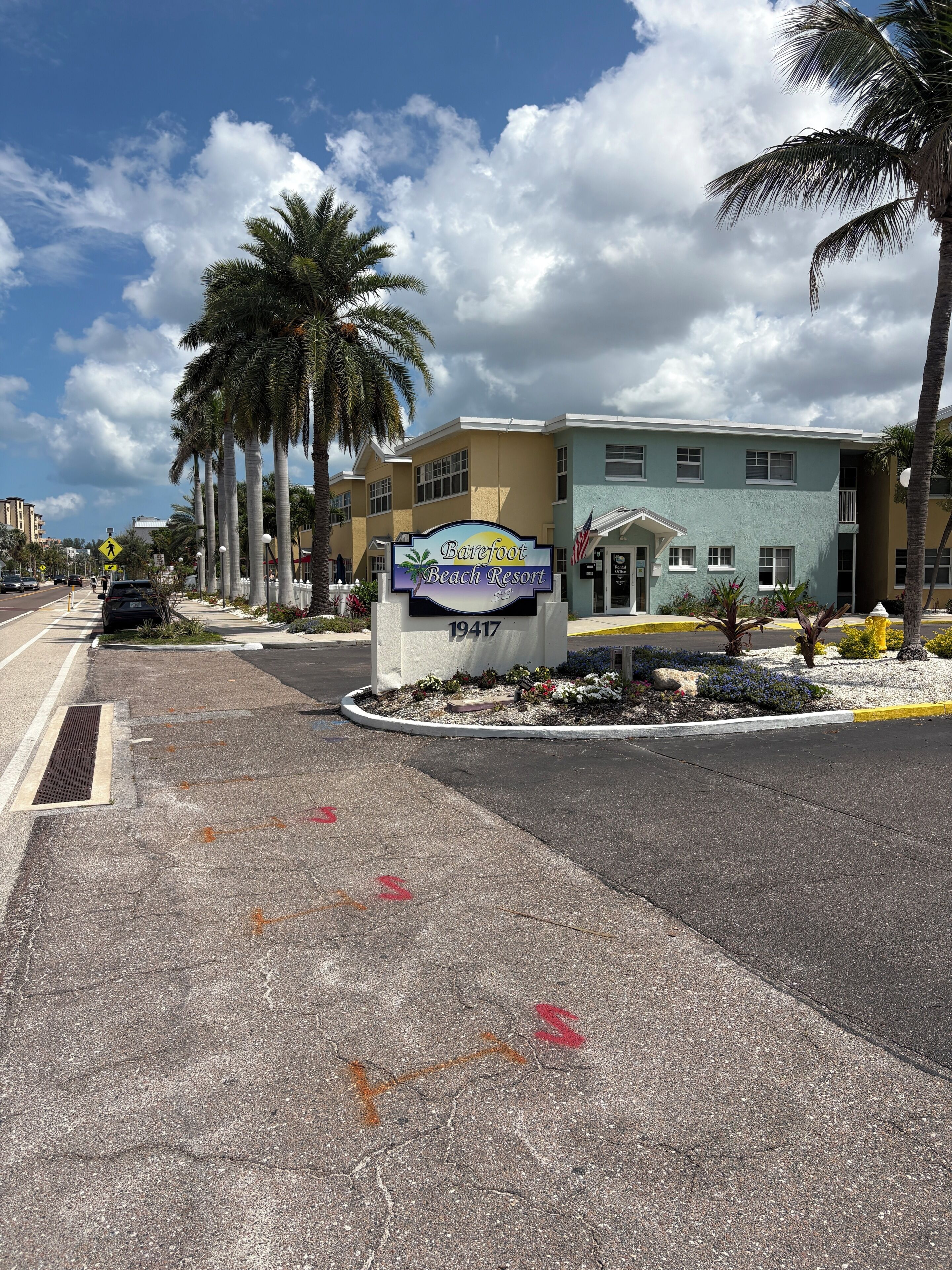A sign for Barefoot Beach Resort with a clear sky and palm trees.