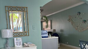 Ein Zimmer mit weißem Konsolentisch, einem Spiegel, einer Wanddekoration und einem Fliesenboden.