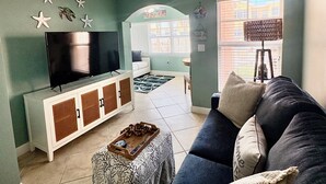 Ein Wohnzimmer mit Deckenventilator, Fernseher, Sofa und einem Fenster mit Jalousien.