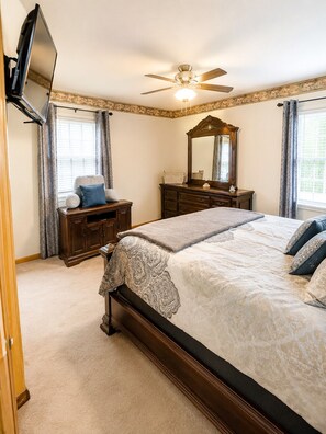 A bedroom with a bed, a dresser, a vanity, a ceiling fan, and a TV mounted on the wall. - Kansas City World Cup  Home W/ Resort Pool outdoor entertainment area sleeps 8 (Leavenworth)