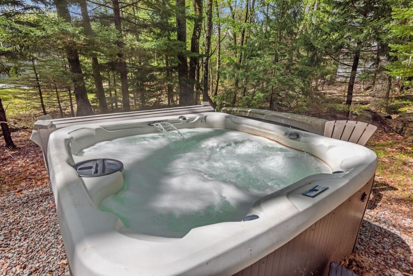 Un jacuzzi en un área boscosa con una terraza de madera y una silla.
