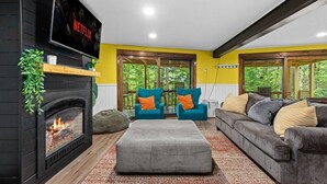 Ein Wohnzimmer mit Kamin, einer Couch, zwei Sesseln und einem Fernseher, der über dem Kamin angebracht ist.