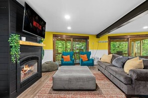 Ein Wohnzimmer mit Kamin, einer Couch, zwei Sesseln und einem Fernseher, der über dem Kamin angebracht ist.
