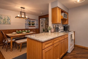 A kitchen with wooden cabinets, a granite countertop, a built-in oven, and a dining area with a table and chairs. - Lake View Lodge/Hot Tub/Game Room/ Grill/Kayak (Lake Harmony)