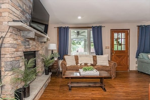 A living room with a stone fireplace, a brown leather sofa, a wooden coffee table, and a blue door. - Lake View Lodge/Hot Tub/Game Room/ Grill/Kayak (Lake Harmony)