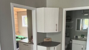 Una habitación con kitchenette, un ventanal pequeño y una puerta que da a otra estancia.