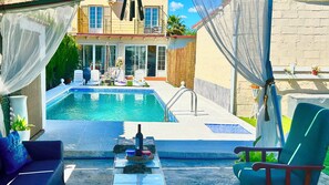 A pool area with lounge chairs, a table with food and drinks, and a building with a balcony. - Marifer Home Private Pool Villa Family Friendly (Las Pajanosas)