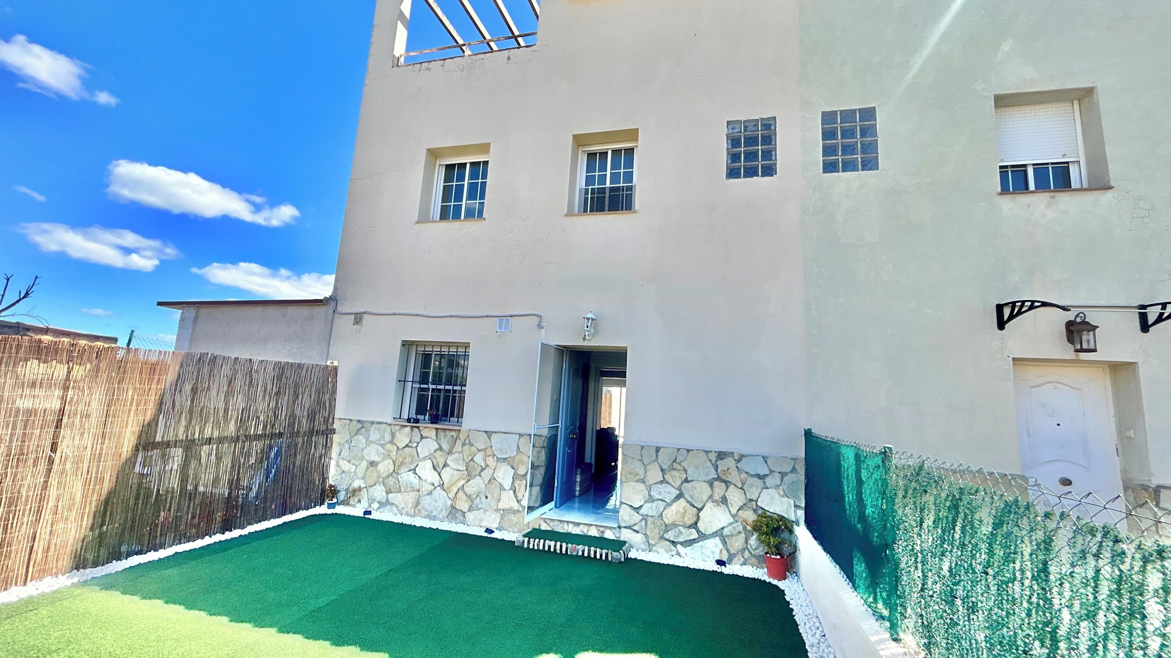 Um edifício de dois andares com base de pedra, várias janelas e uma pequena área externa com grama sintética.