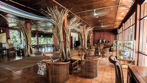 Un espacio interior amplio con muebles de madera, ventanas grandes y plantas decorativas.