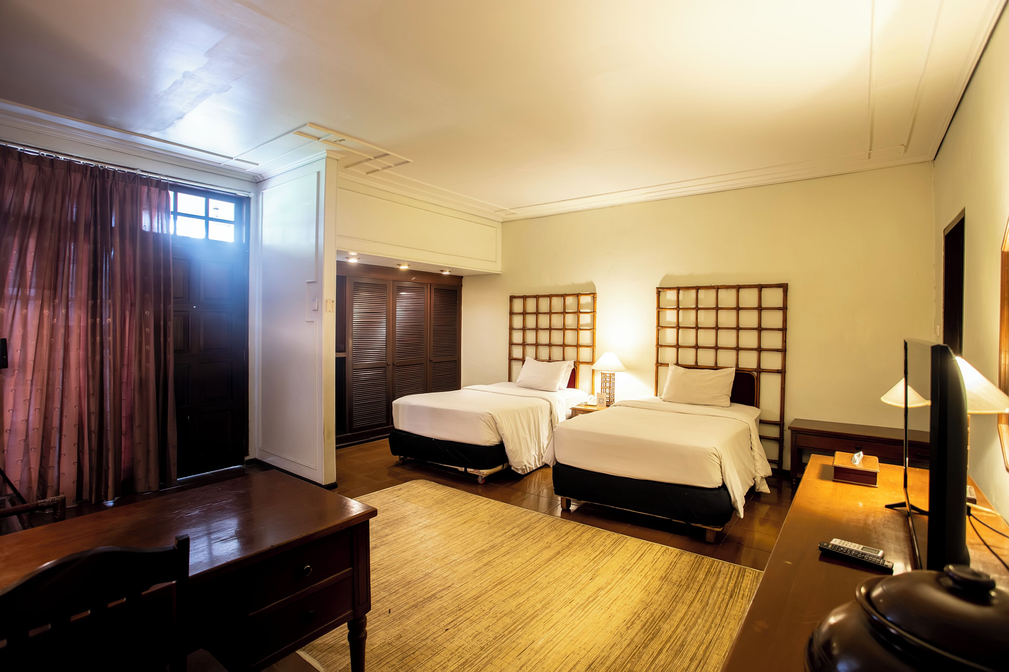 A hotel room with two beds, a desk, a chair, a television, and a window with curtains.