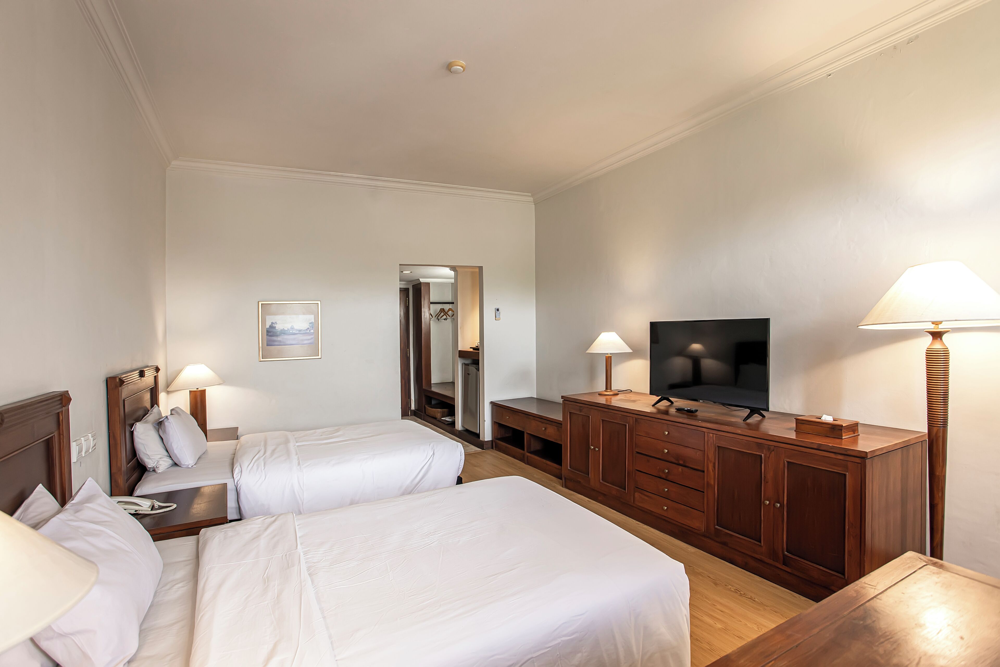 A hotel room with two beds, a TV, wooden furniture, and a mirror.