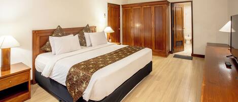 A hotel room with a large bed, wooden wardrobe, bedside tables, and a television.