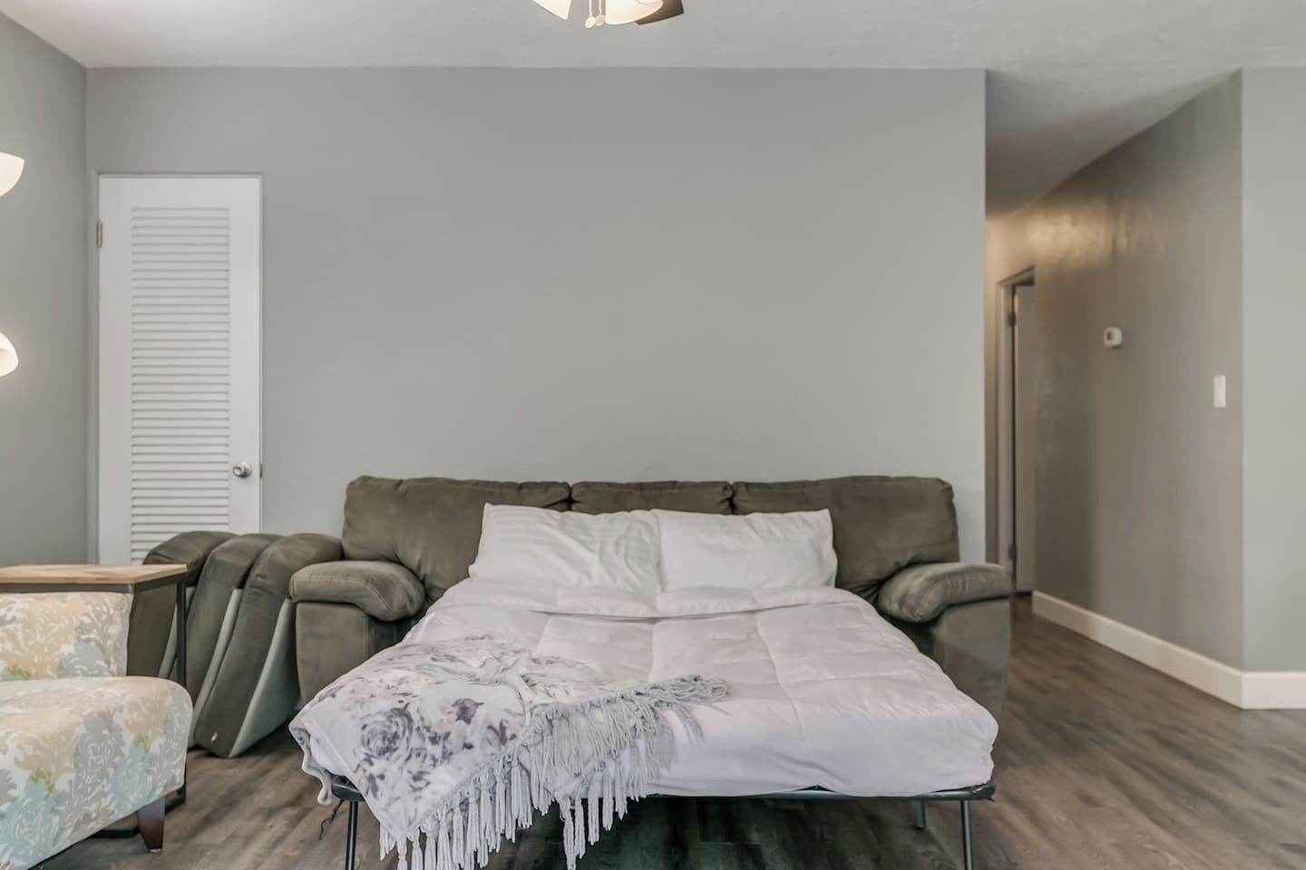Ein Schlafzimmer mit einem Bett, einem Nachttisch, einem Sessel und einer Tür.