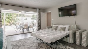 Een slaapkamer met een bed, een televisie, een bank en uitzicht op een buitengebied met een tafel en stoelen.