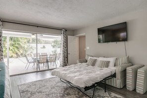 Ein Schlafzimmer mit Bett, Fernseher, Sofa und Blick auf einen Außenbereich mit Tisch und Stühlen.