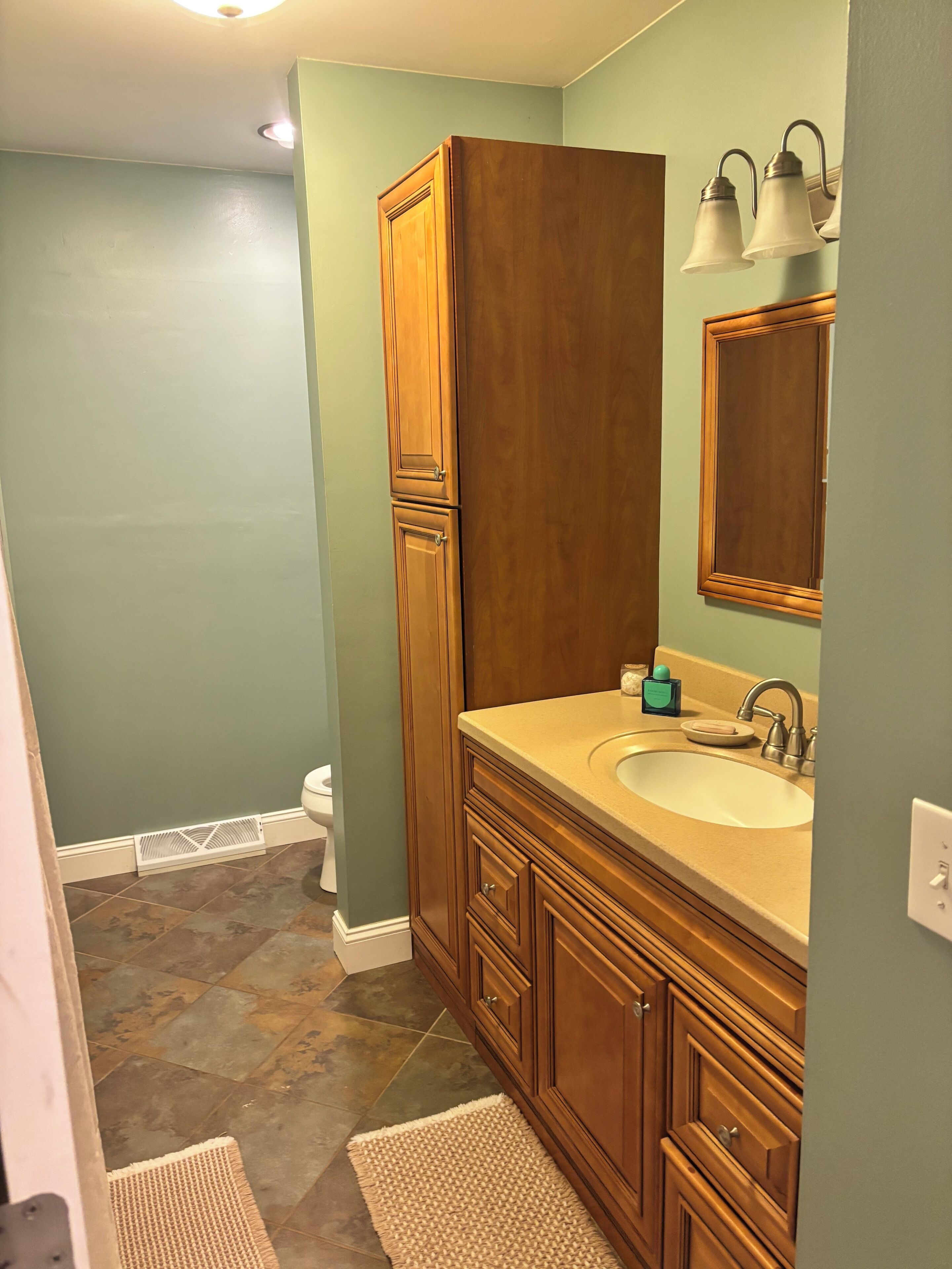 A bathroom with a wooden vanity, a sink, a mirror, and a light fixture.