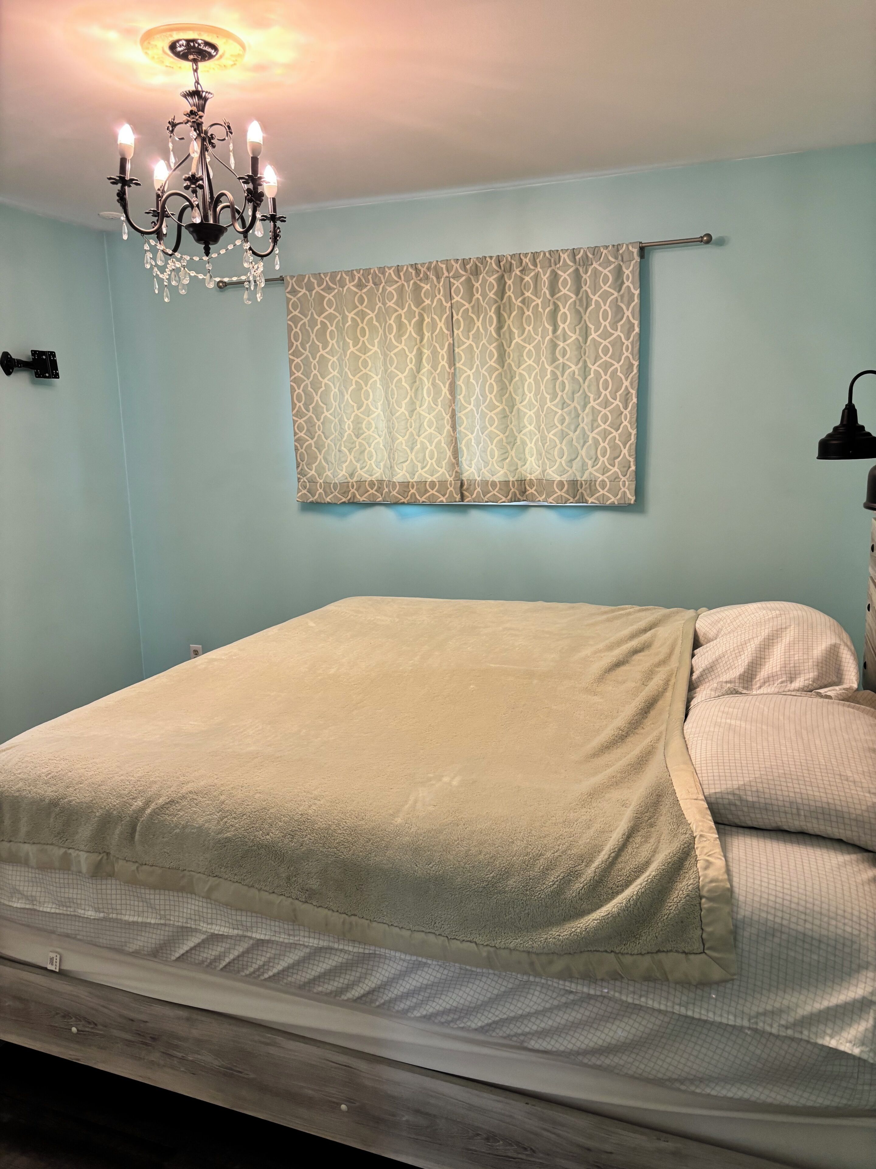 Een slaapkamer met een bed, een kroonluchter, een gordijn met patroon en een bedlamp.