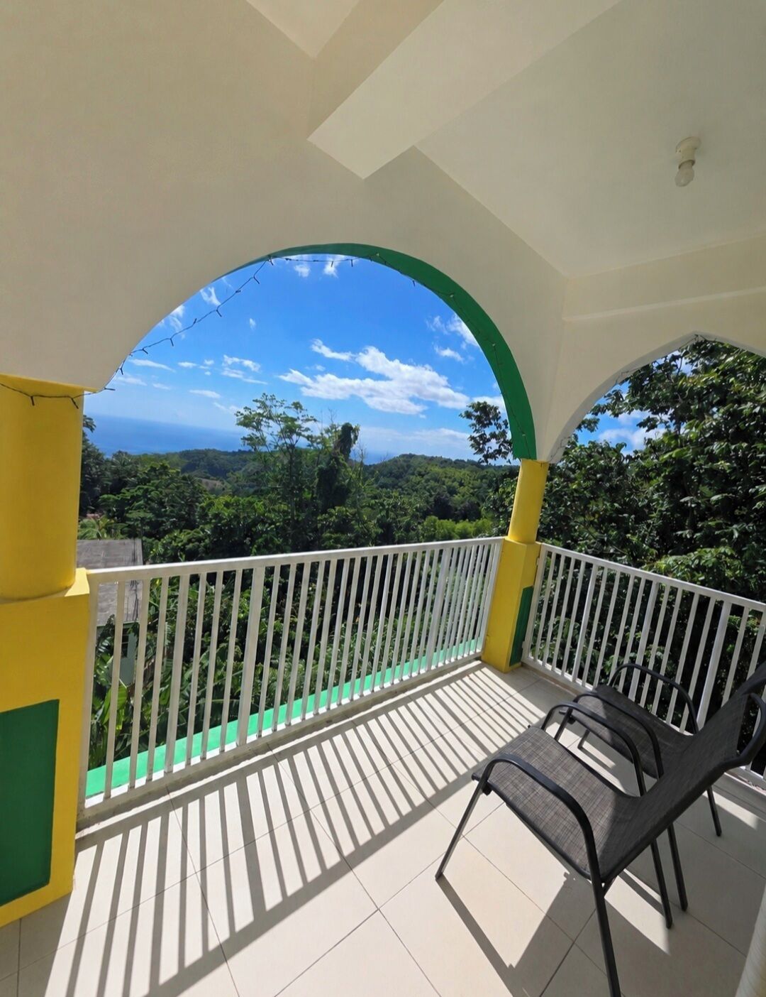 Un balcón con barandilla blanca, vistas a un paisaje verde y cielo despejado.