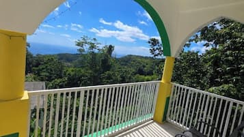 Un balcón con barandilla blanca, vistas a un paisaje verde y cielo despejado.