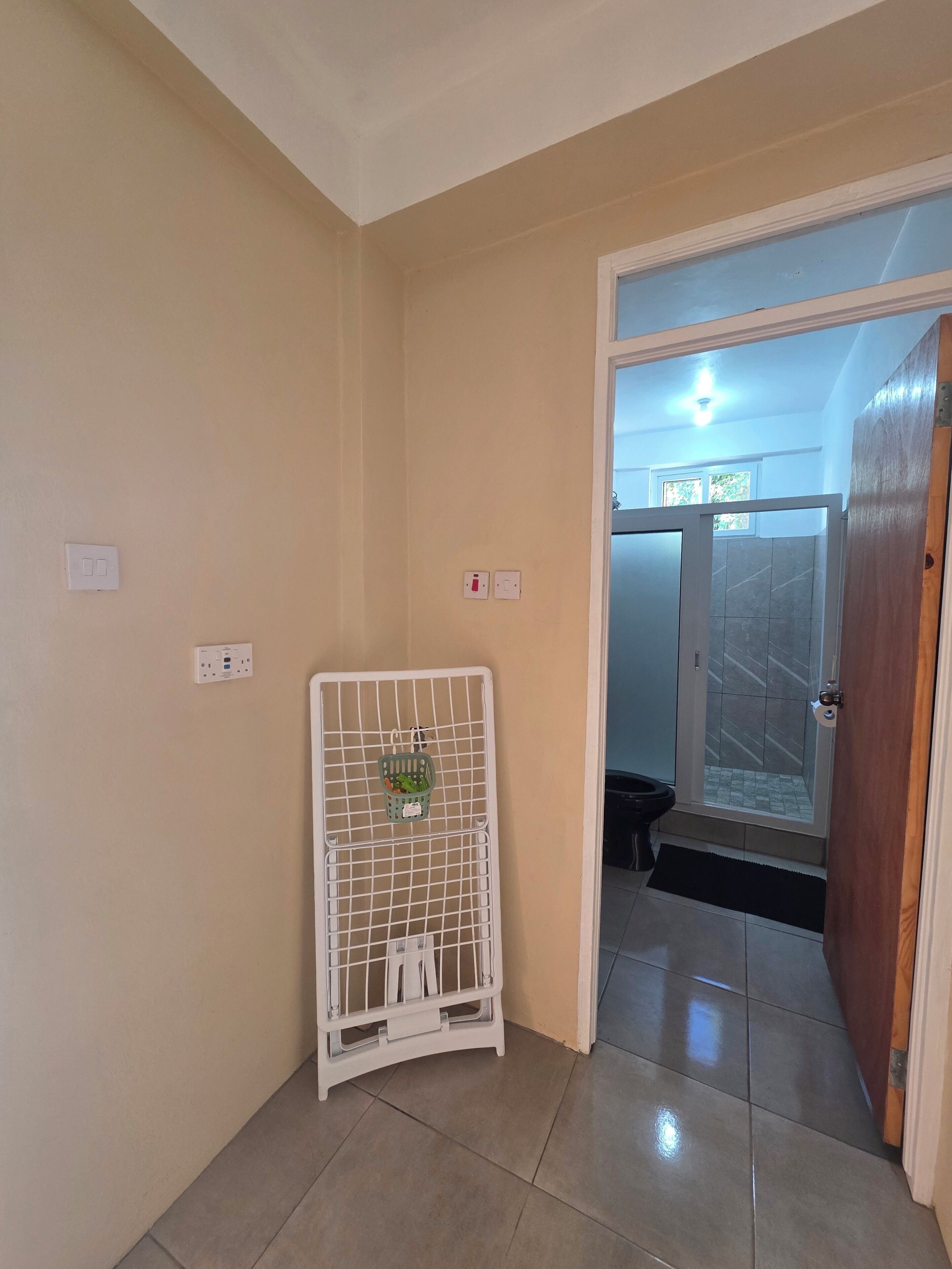 Un pasillo con una puerta blanca, una pared blanca con interruptor de luz y una zona de ducha con puerta de cristal.