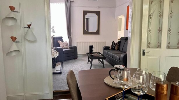 A dining area with a table set for four, a mirror, and a view into a living room with a sofa and a coffee table. - Spacious Home - Sleeps 5 Persons (Liverpool)