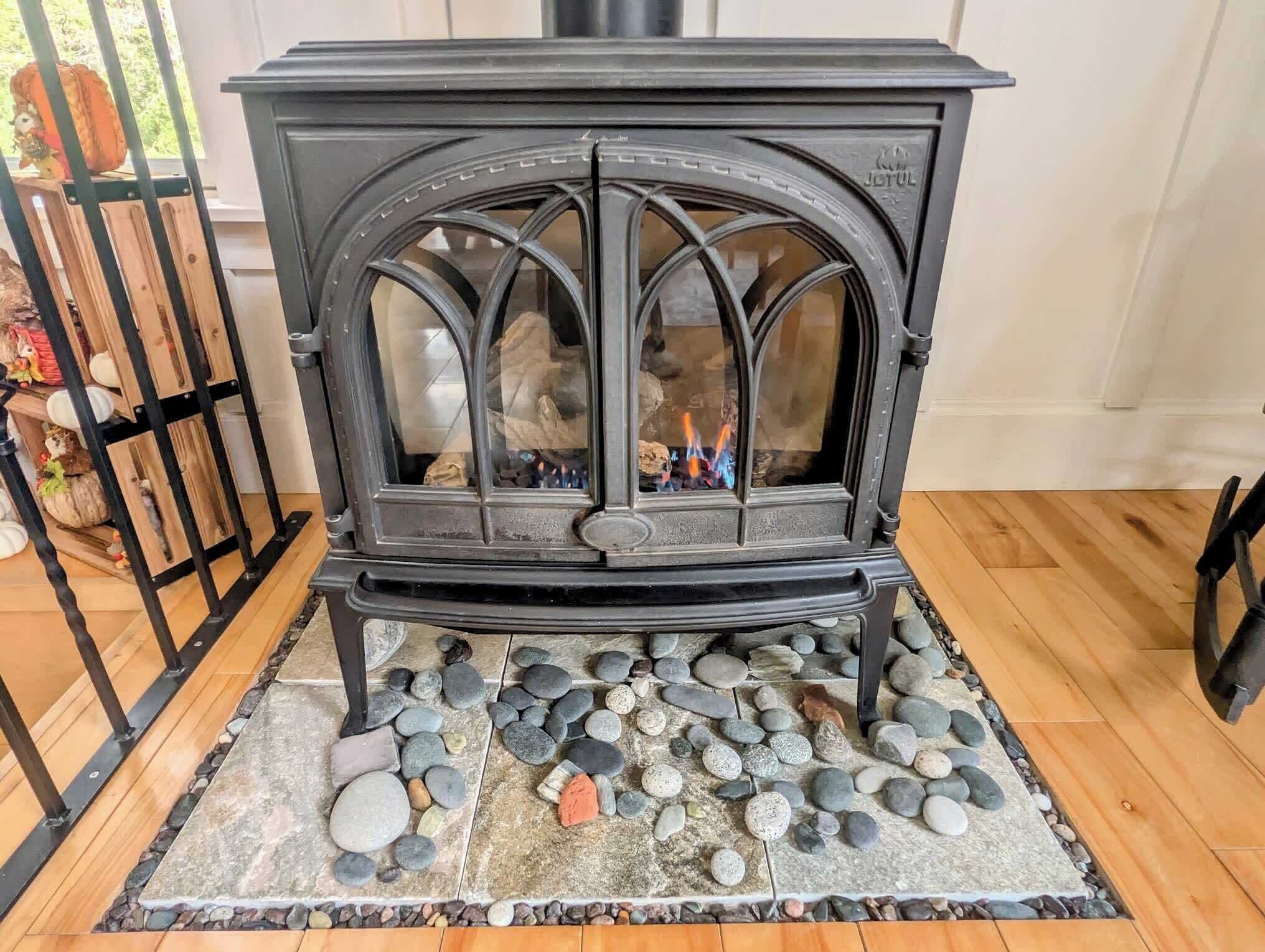 A black wood-burning stove with a stone base, set in a room with wooden flooring and a metal gate.