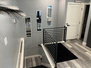 Uma escadaria com corrimão de metal preto, tapete preto e porta branca com a placa 'welcome'.
