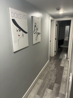 A hallway with a grey wall, wooden flooring, and two framed artworks.
