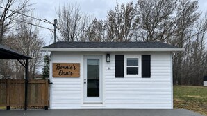A small white house with a wooden deck, a sign reading 'Bonnie's Oaas,' and a number '52' on the door. - Cozy cottage River view, close to beaches and amenities. (Grand Barachois)