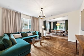 Ein Wohnzimmer mit Ecksofa, einer Essecke mit Tisch und Stühlen sowie einer Deckenleuchte.
