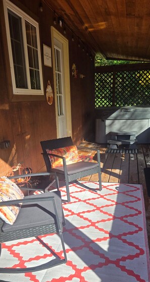 Ein Außenbereich mit einer Holzterrasse, zwei Stühlen mit Kissen, einem Tisch und einem Grill.