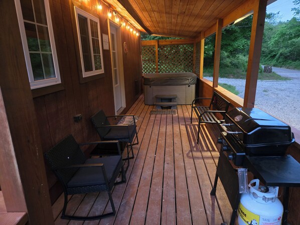 A wooden deck with a grill, seating, and a hot tub.