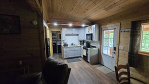 Een blokhutinterieur met een keuken, eethoek en een deur die uitkomt op een balkon.