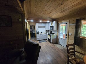 A cabin interior with a kitchen, dining area, and a visible door leading to a balcony.