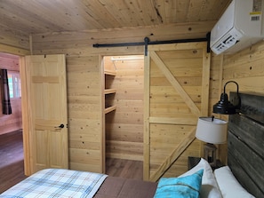 A wooden interior with a bed, a nightstand, a lamp, and a closet.