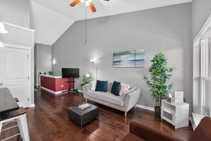 Un salon avec un canapé, une table basse, un téléviseur et une plante.