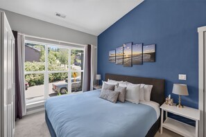 Een slaapkamer met een groot bed, nachtkastje, lamp en raam met gordijnen.