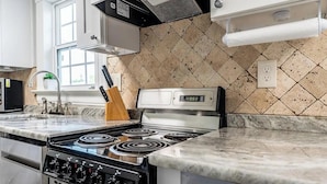 A kitchen with a gas stove, a knife block, and a digital clock.