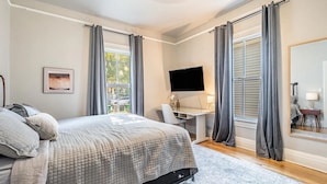 A bedroom with a bed, a desk, a TV, and a large mirror.