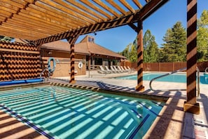 A pool area with a wooden pergola, lounge chairs, and a building with a brick facade. - 2 Min Walk To Ski*Hot Tub, Pool, Gym, Modern (Park City)
