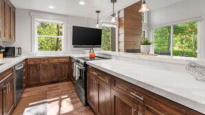 A modern kitchen with wooden cabinets, a large island, a built-in oven, and a TV mounted above the island. - 2 Min Walk To Ski*Hot Tub, Pool, Gym, Modern (Park City)