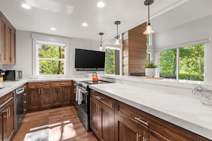 A modern kitchen with wooden cabinets, a large island, a built-in oven, and a TV mounted above the island. - 2 Min Walk To Ski*Hot Tub, Pool, Gym, Modern (Park City)