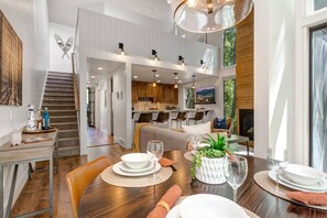 A spacious dining area with a wooden table set for a meal, a kitchen in the background, and a staircase leading to an upper level. - 2 Min Walk To Ski*Hot Tub, Pool, Gym, Modern (Park City)
