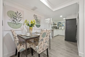 Et spiseområde med et glasbord, mønstrede stole, en vase med blomster og abstrakt vægkunst.