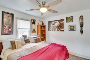Un dormitorio con cama, ventilador de techo, ventana y decoración en la pared.
