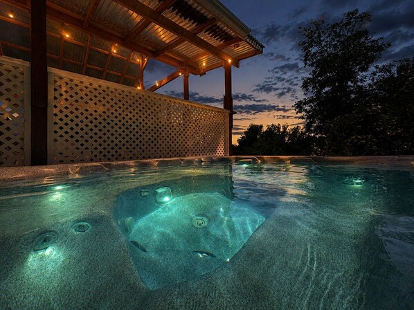 A swimming pool with a wooden deck and a covered area with string lights.