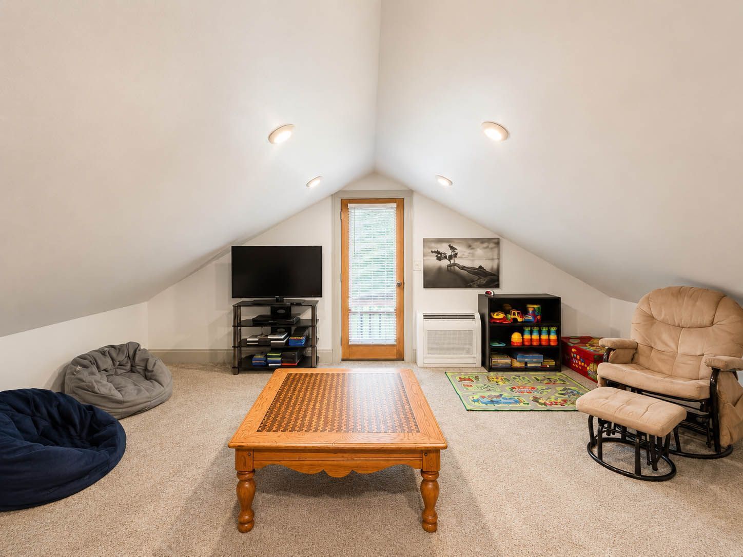 A cozy attic room with a wooden table, bean bag, and a bookshelf with toys.